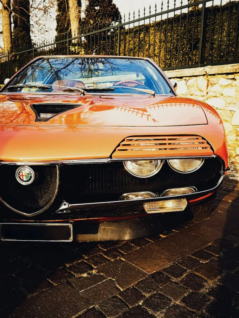 orange classic car parked beside brick wall